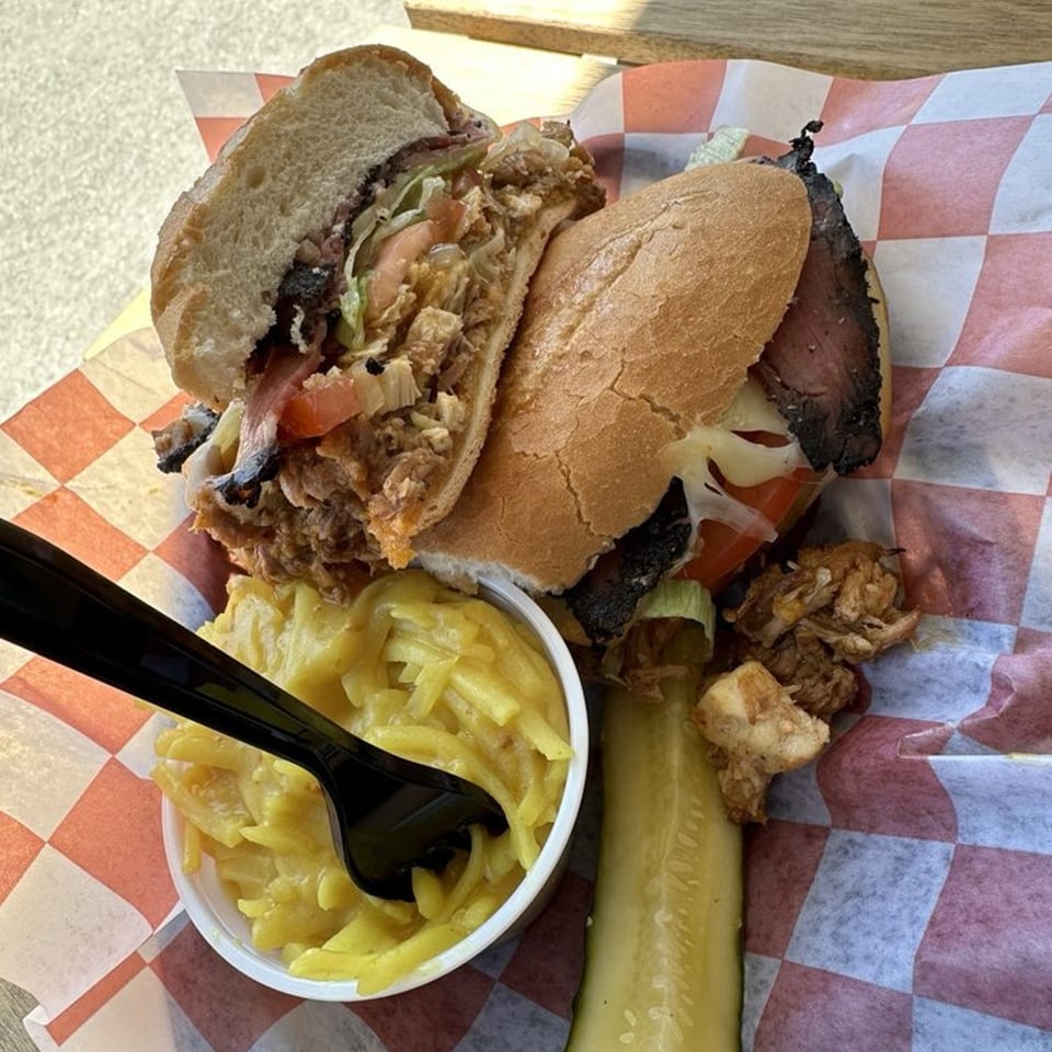 Two sandwiches, a side of macaroni salad, and a pickle spear on checkered paper.