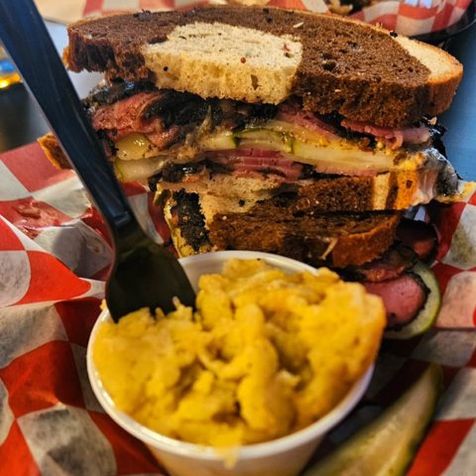 A towering pastrami sandwich on rye bread with a side of mac and cheese.