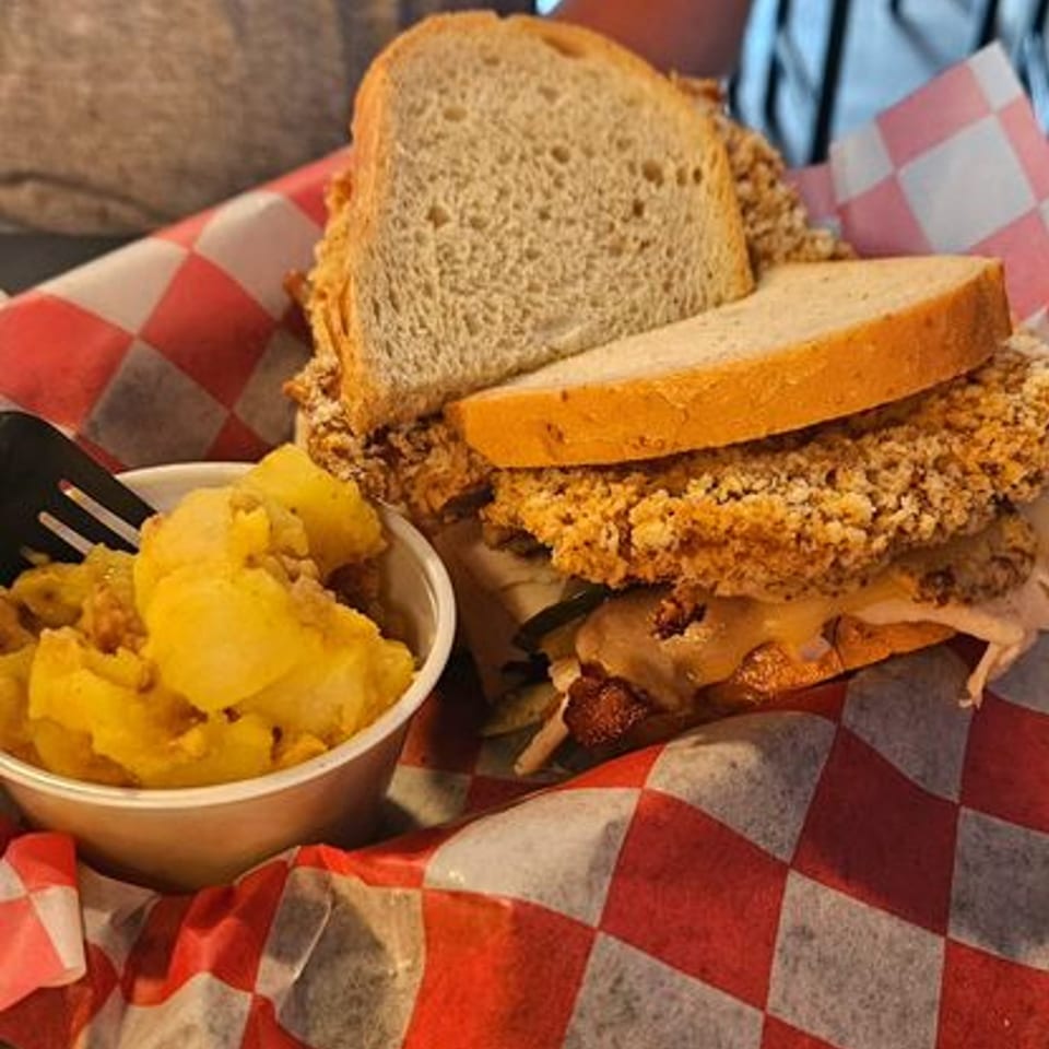 A German schnitzel sandwich with bacon and cheese, served with a side of potato salad.
